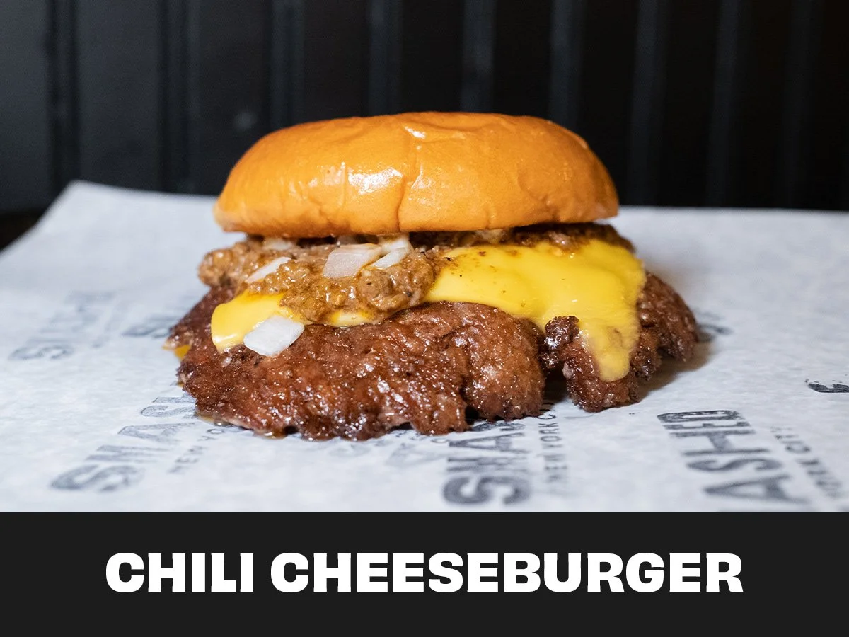 Close-up of a chili cheeseburger with melted cheese, ground beef patty, chopped onions, and a bun on top, served on white paper with black text.