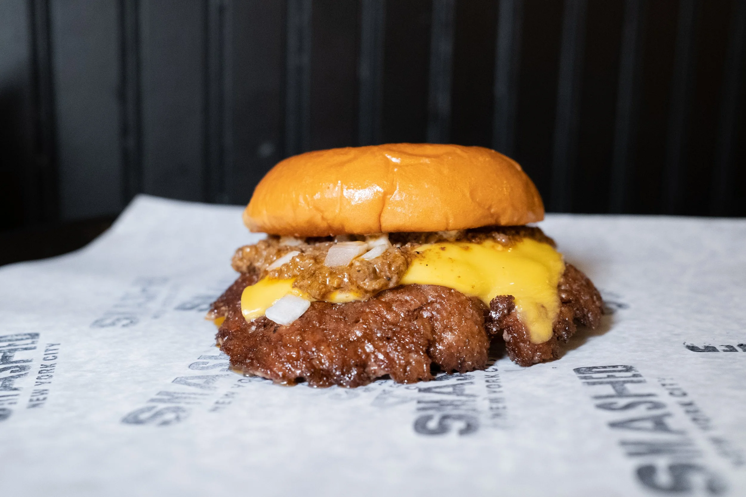 Cheeseburger with cheese, cooked ground beef patty, onions, and ground beef on a bun, placed on branded paper.