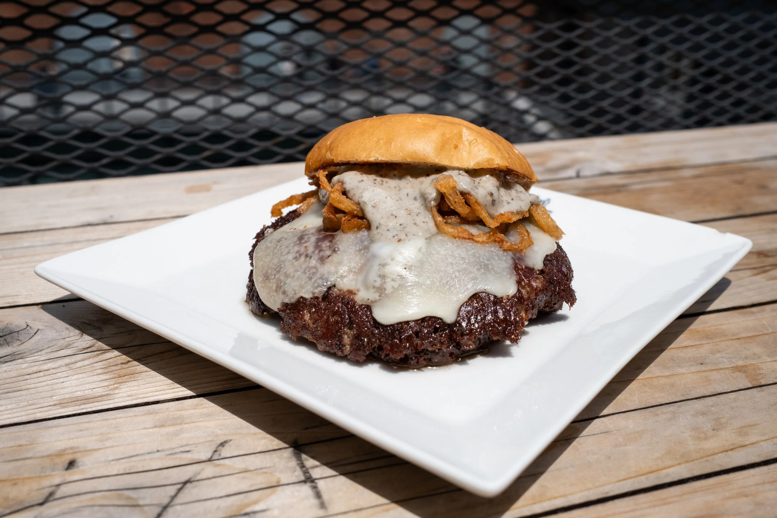 Hamburger with melted cheese, crispy fried onions, and a toasted bun served on a white square plate outside on a wooden table.