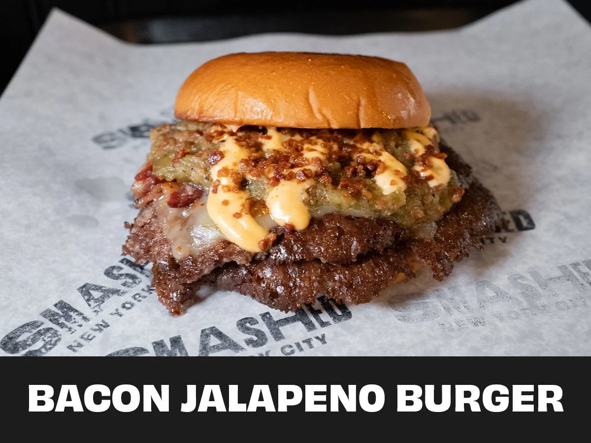 Close-up of a bacon jalapeno burger with a beef patty, jalapenos, mayonnaise, and a toasted bun on branded paper.
