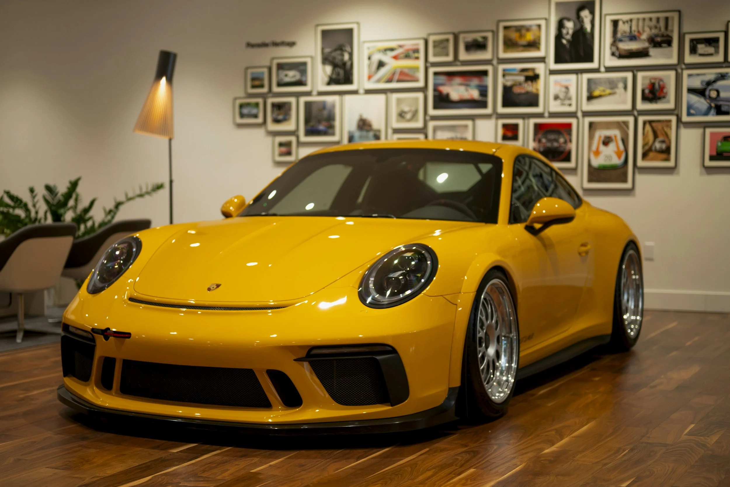 Yellow Porsche sports car inside a modern gallery with framed photographs on the wall.