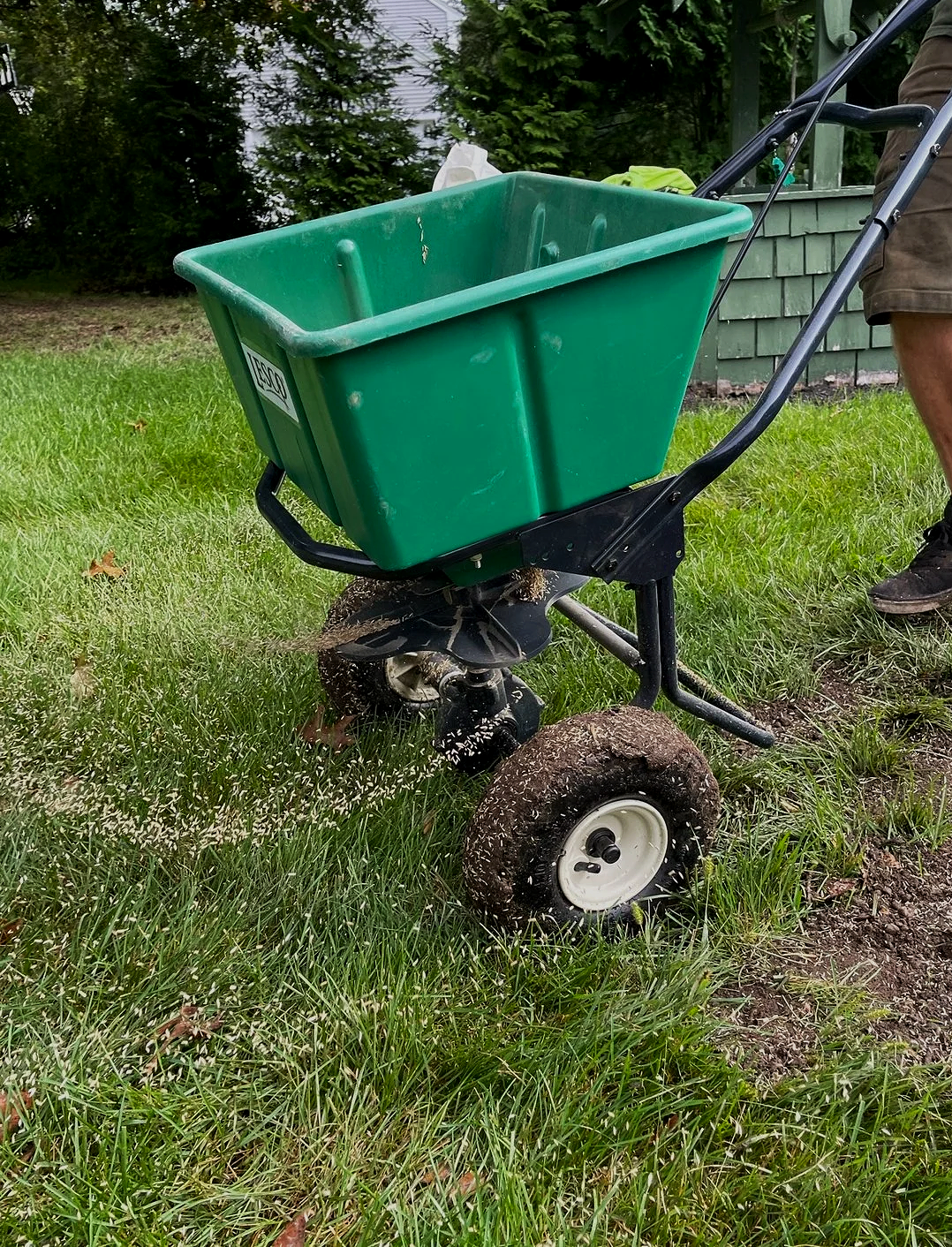 Green wheelbarrow with a black metal frame and large dirt-covered wheel, being pushed on a grassy lawn.