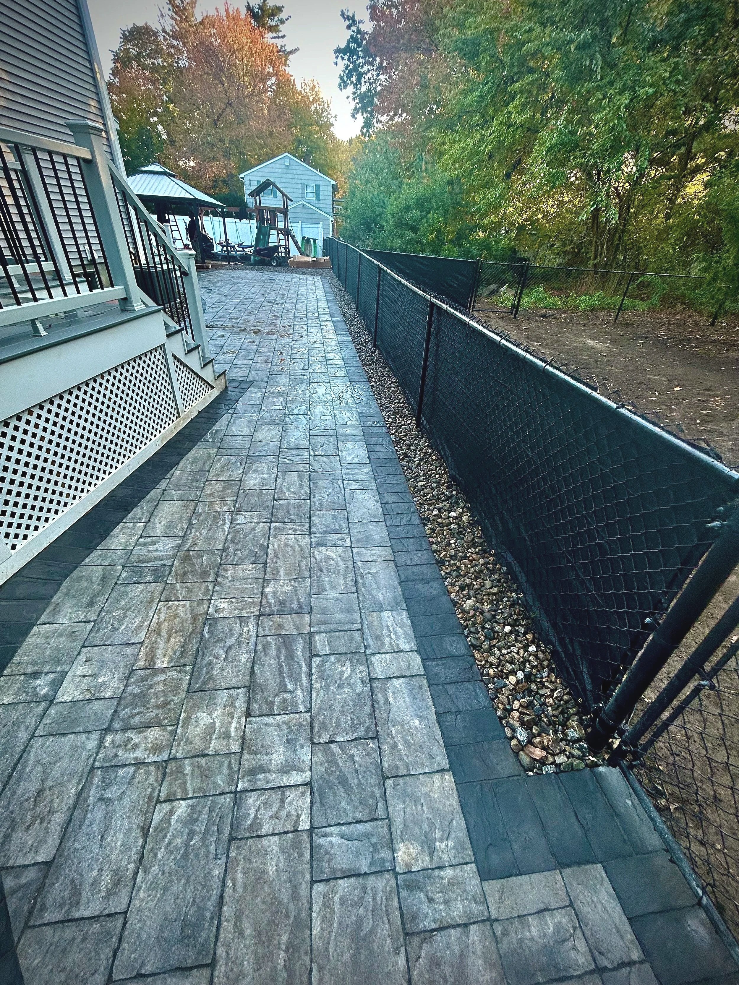 A patio with stone pavers, a black fence, and outdoor furniture in a backyard with trees