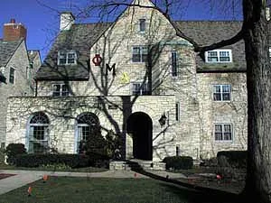 An old stone building with multiple windows and an arched entrance, surrounded by leafless trees and small orange cones on the grass.