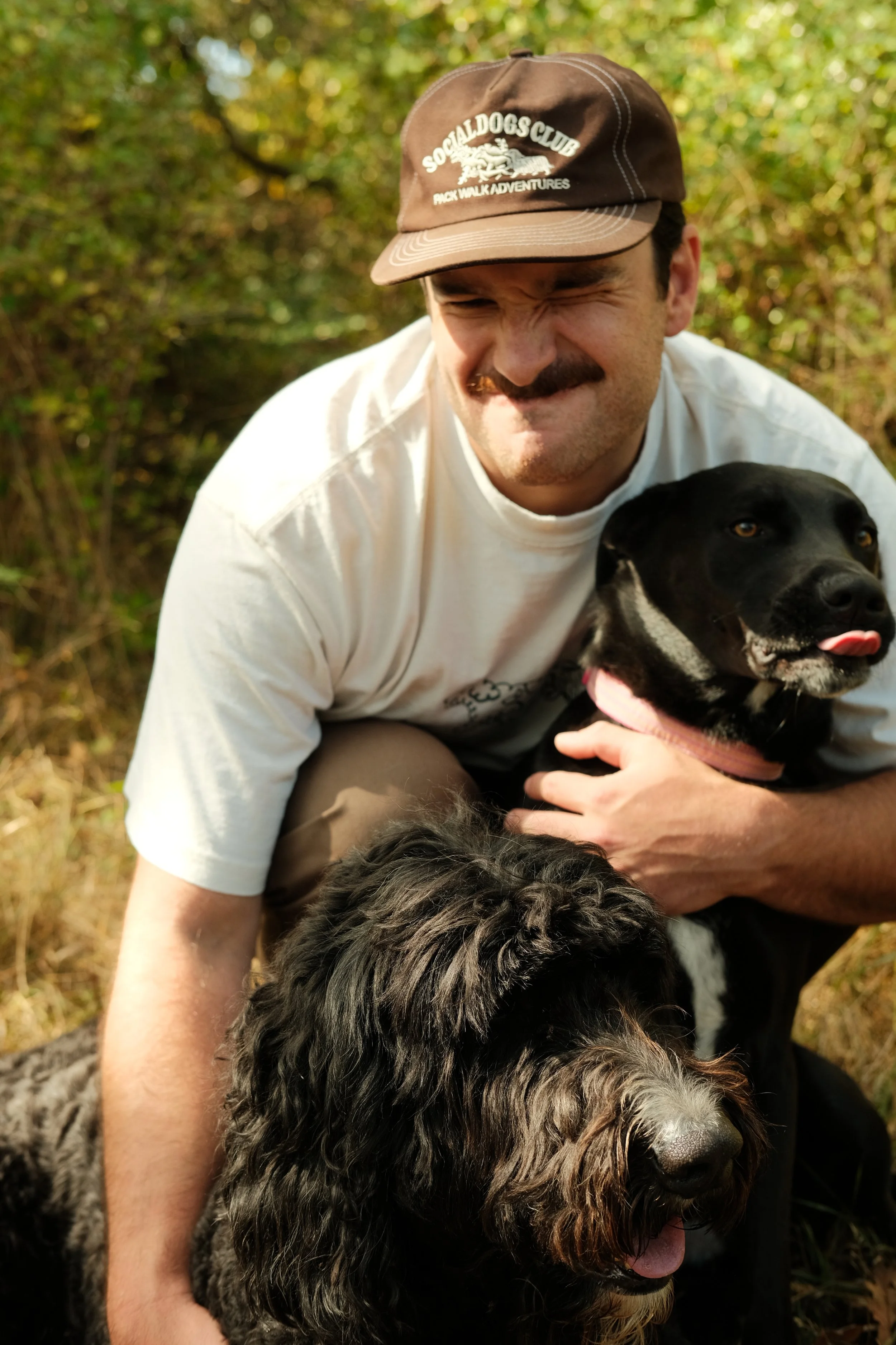 Jake smiling with Frankie and Winston the dogs licking his face.