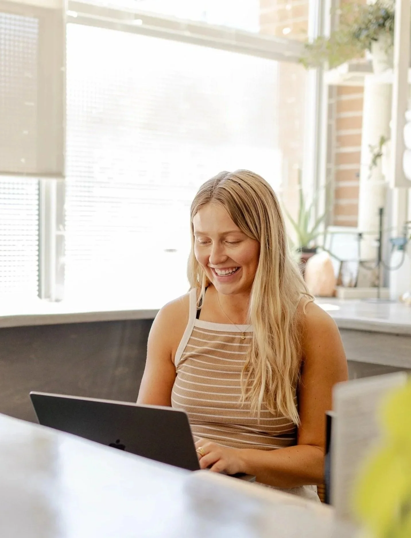 Aubrey, our Marketing + Admin Director, working on a laptop and laughing at her desk.