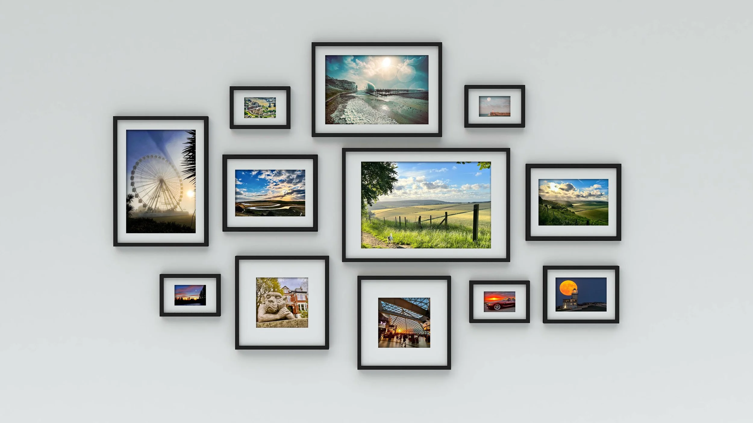 A gallery wall with 13 framed photos of various landscapes, a ferris wheel, city scenes, and a moonlit sky on a white wall.