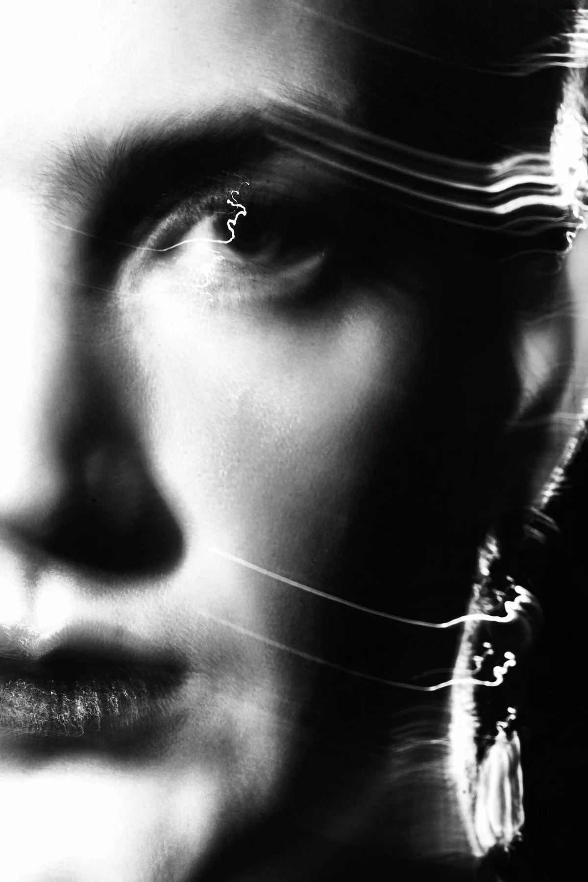 Close-up of a person's face, focusing on the eye and lips, with abstract light streaks and ripples in black and white.