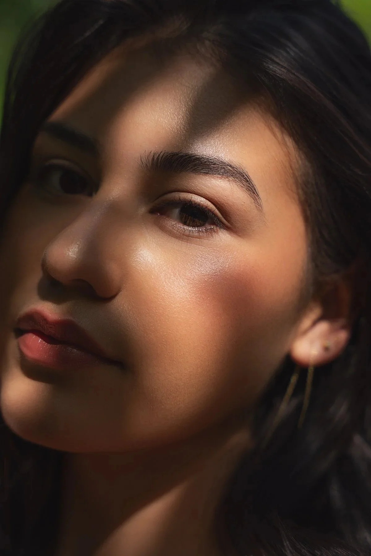 Close-up of a woman's face with smooth skin, dark hair, and subtle makeup, focusing on her eye, cheekbone, and lips.