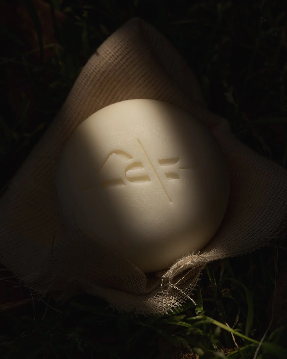 A white egg with a slash and the number 25 cut into its surface, wrapped in fabric and placed on grass, illuminated by sunlight.