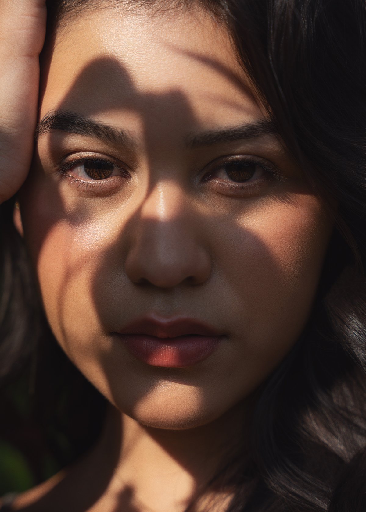 Close-up of a woman's face with a shadow from her hand on her forehead, sunlight highlighting her skin and features.