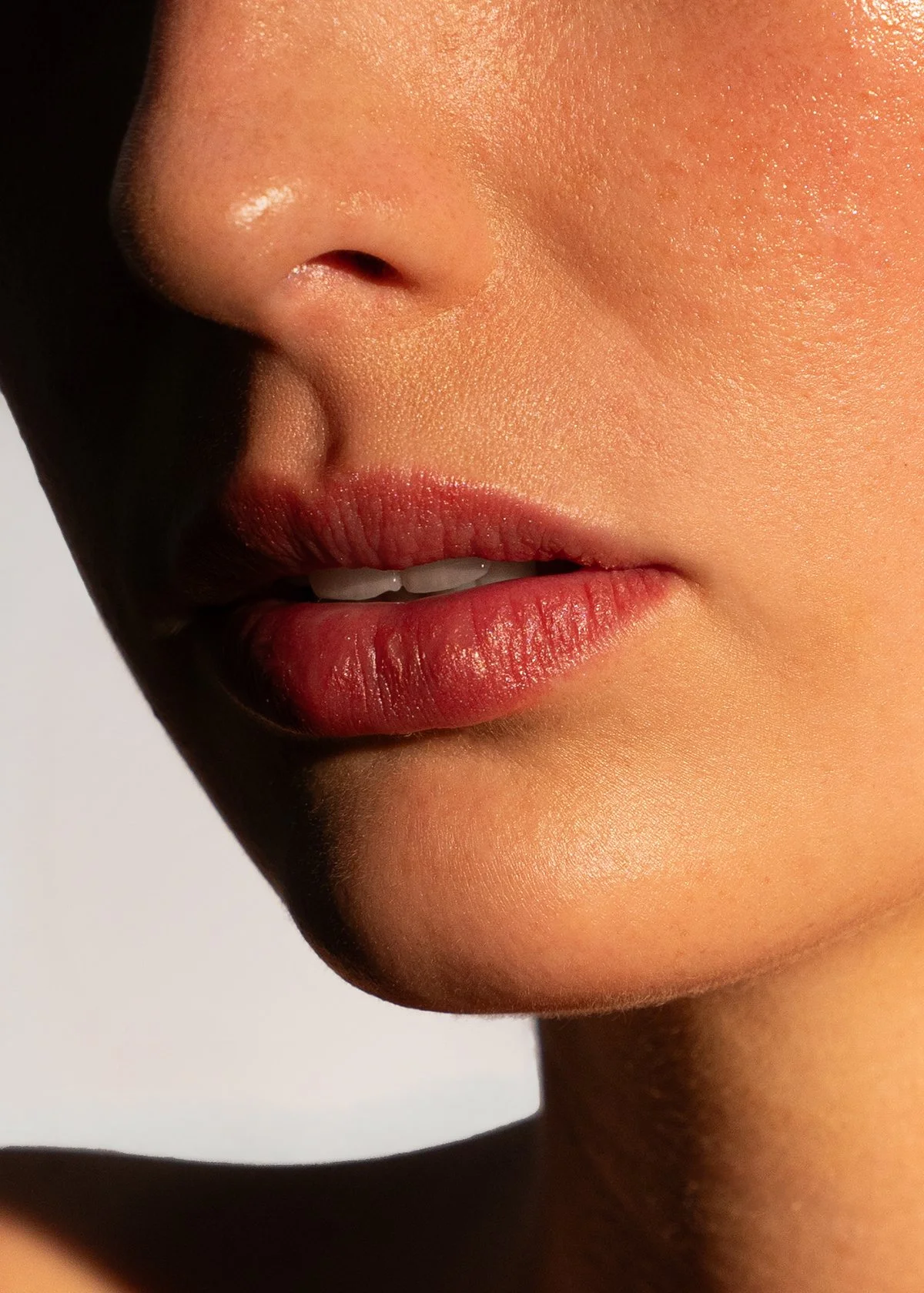 Close-up of a person's lips and nose, with smooth skin, slightly parted lips, and a hint of teeth showing.