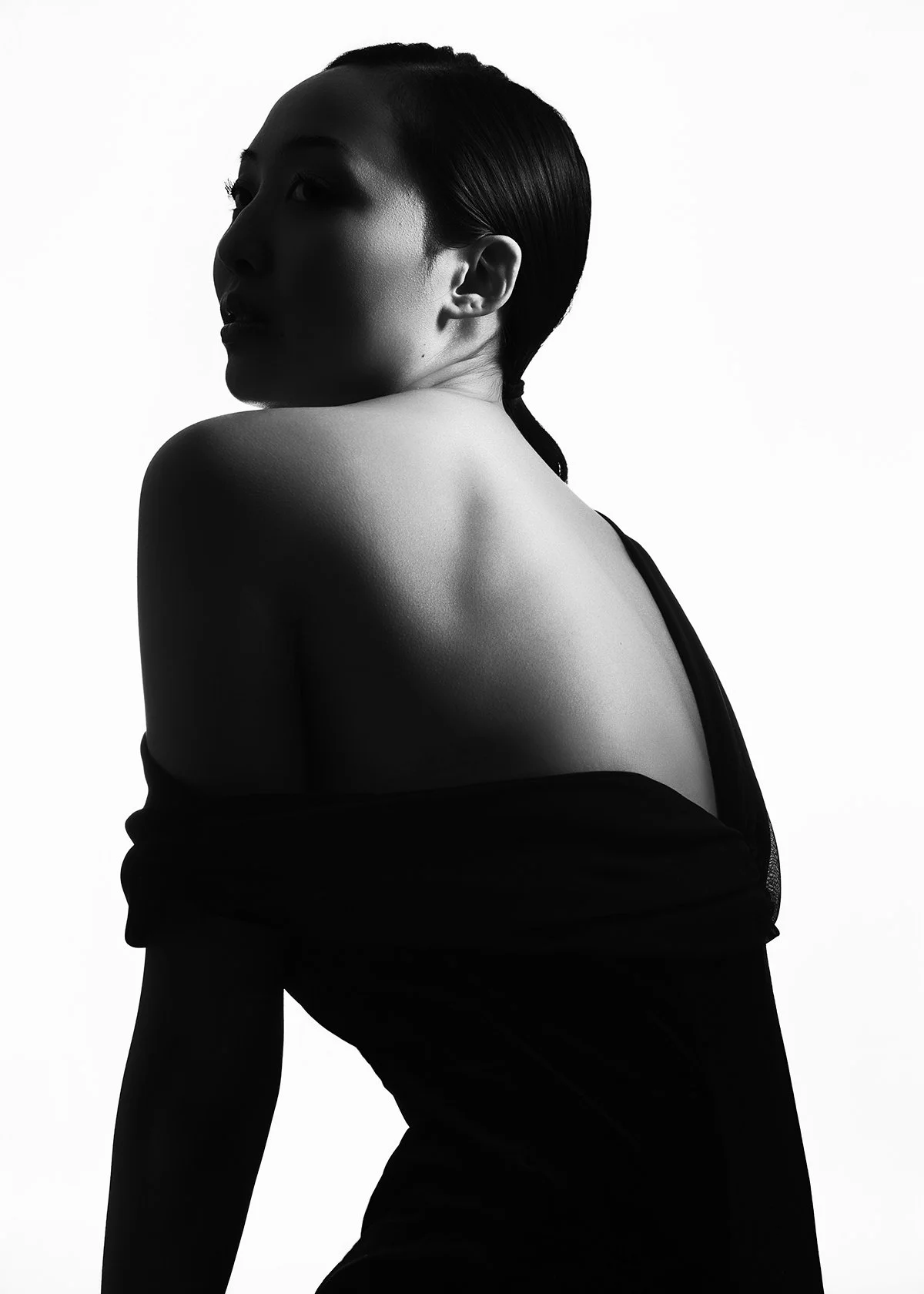 Black and white photo of a woman with dark hair, turned to the side, showing her shoulder and profile.