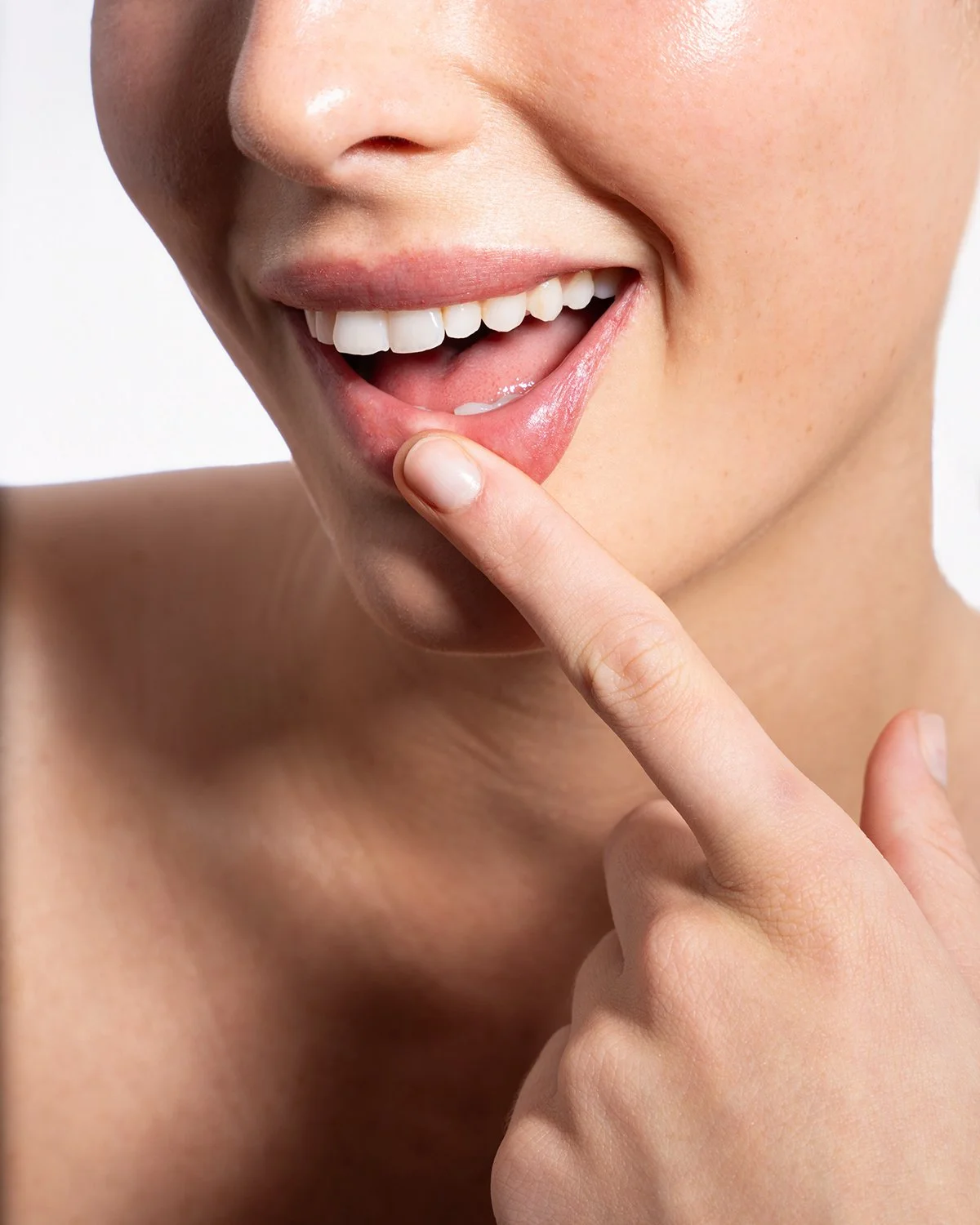 Close-up of a smiling woman with her finger on her lips, wearing minimal makeup.