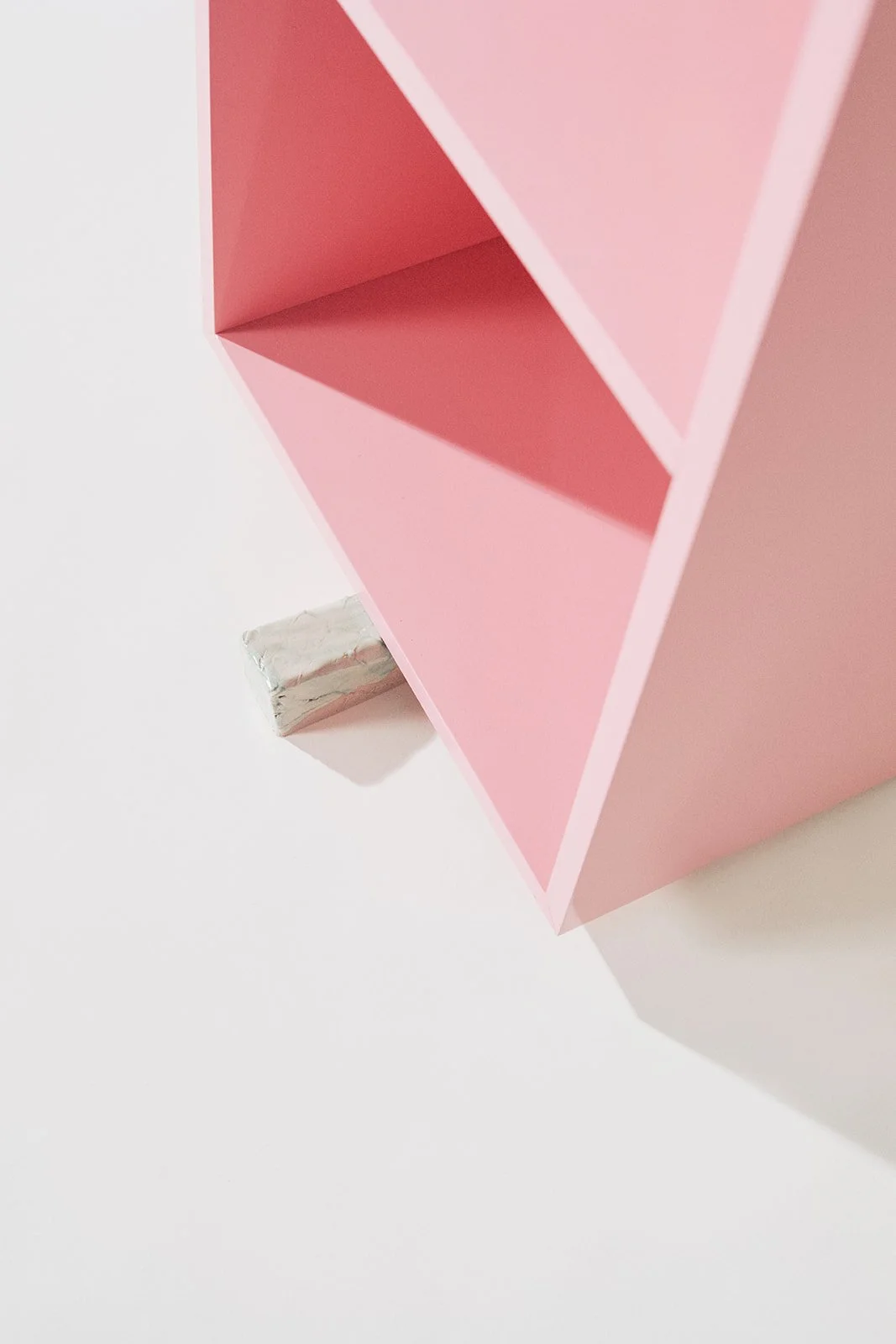 Close-up of a pink bookshelf with three empty shelves, mounted on a white wall, with a small silver object on the floor underneath.
