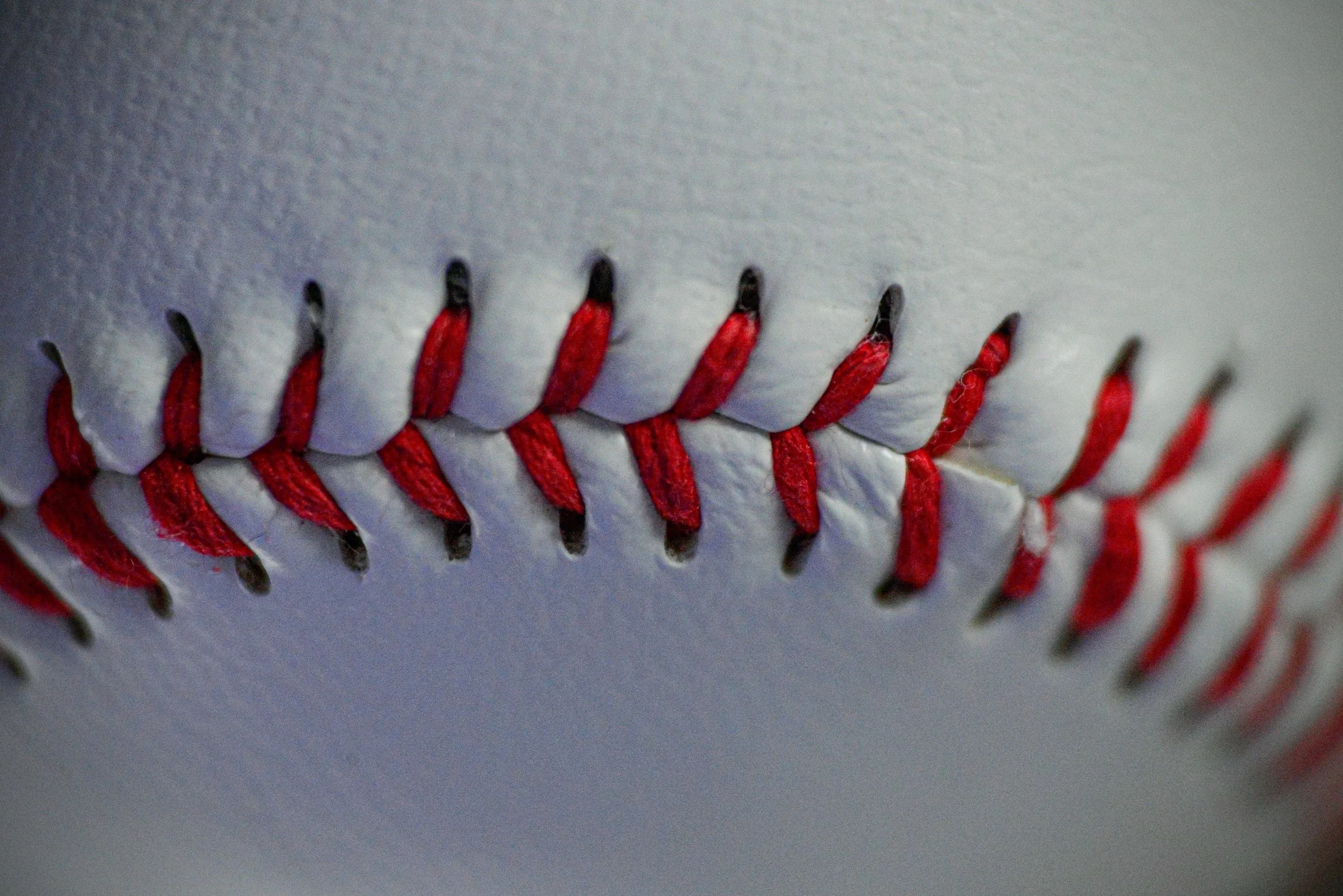 Close-up of a baseball's red stitched seam against the white leather surface.