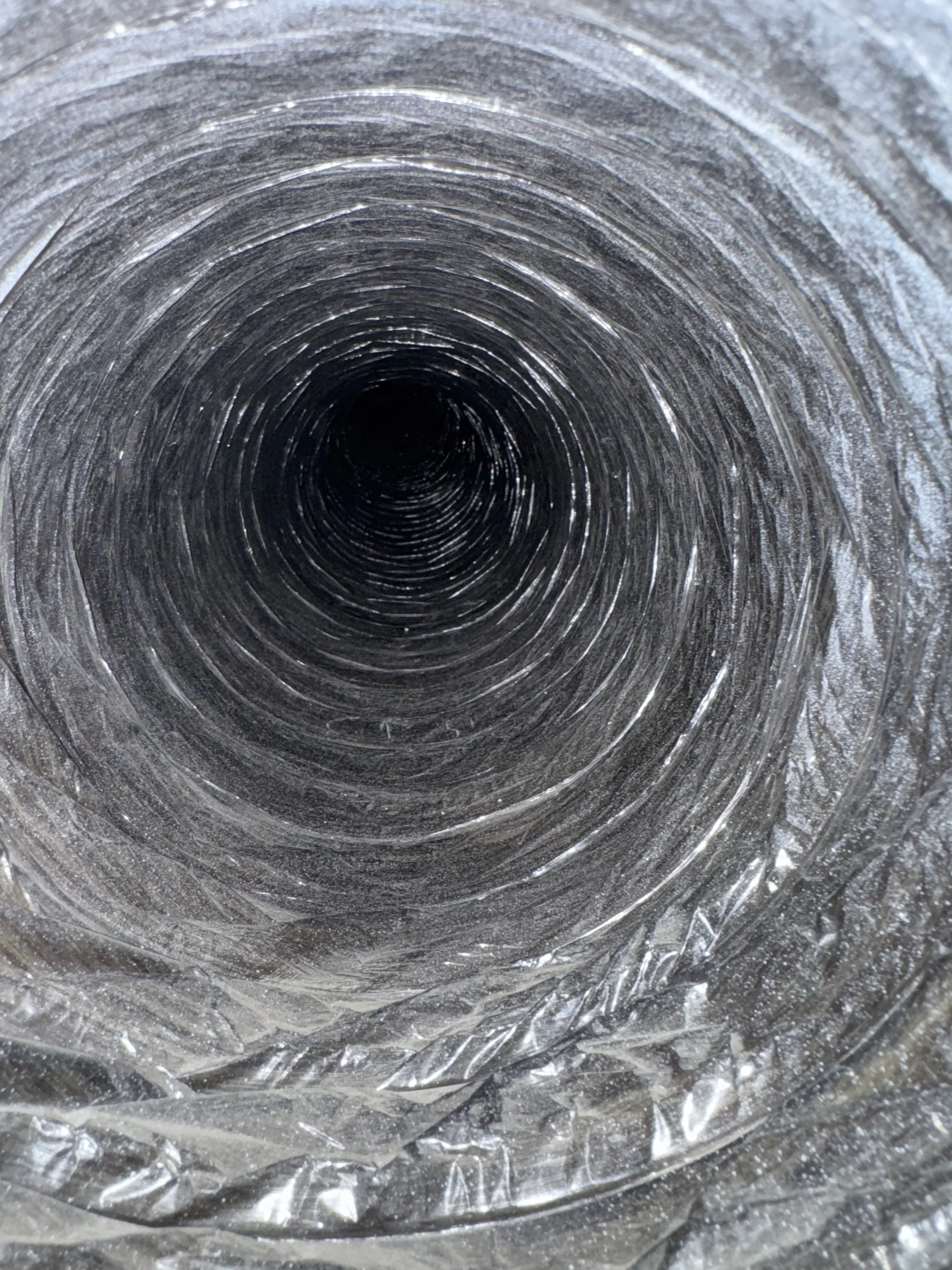 Close-up view looking inside a metallic duct or pipe, showing concentric rings and textured surfaces.