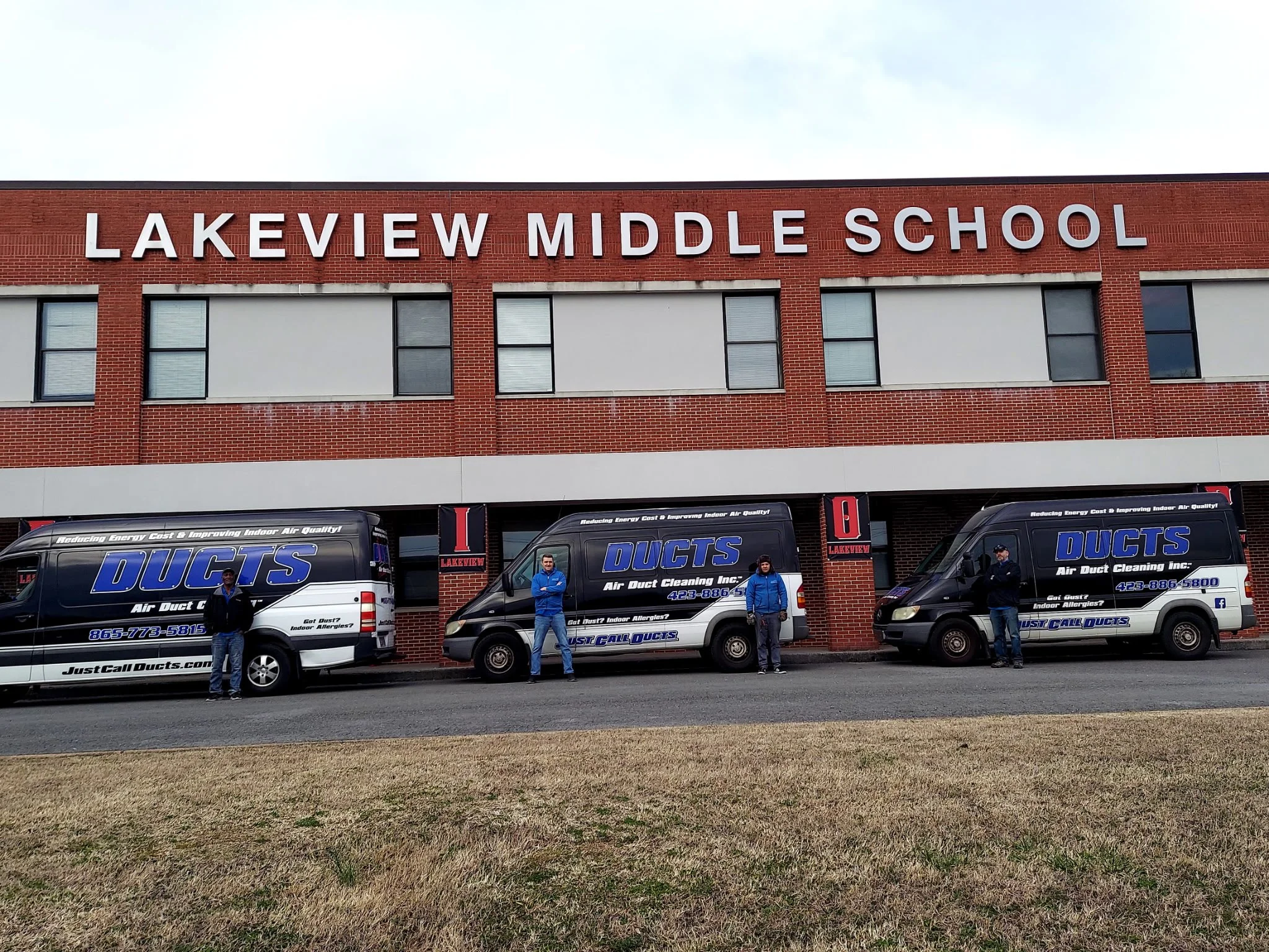 Three branded vans parked in front of Lakeview Middle School building with four people standing next to each van.