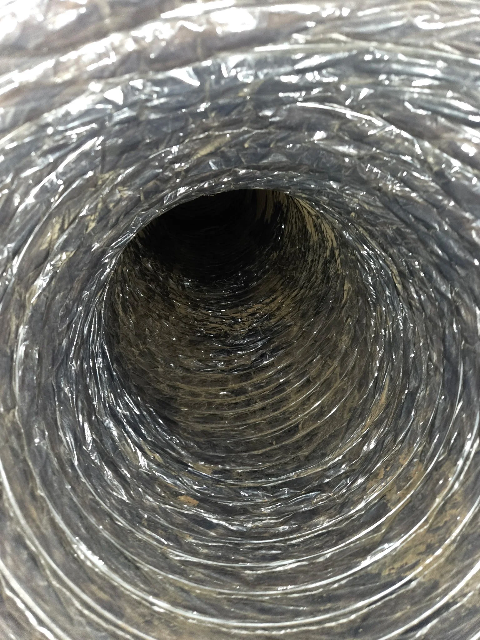 View inside a metallic, reflective, flexible duct, showing its circular shape and spiral ridges.