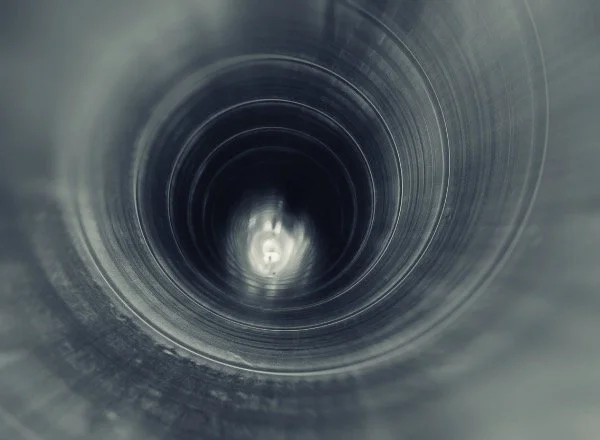 Inside view of a dark, cylindrical pipe or tunnel, looking towards the opening at the other end