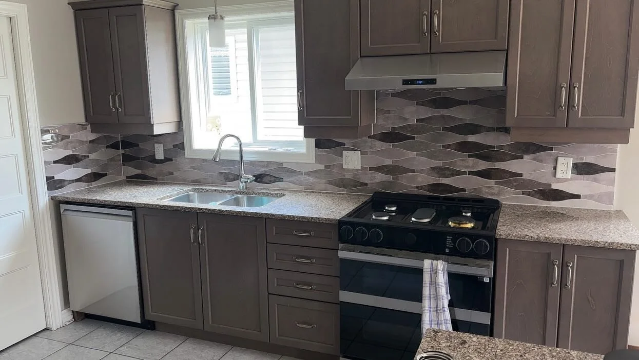 Kitchen with gray cabinets, granite countertop, tile backsplash with wavy patterns, a window above the sink, a black stove, and a small white refrigerator.