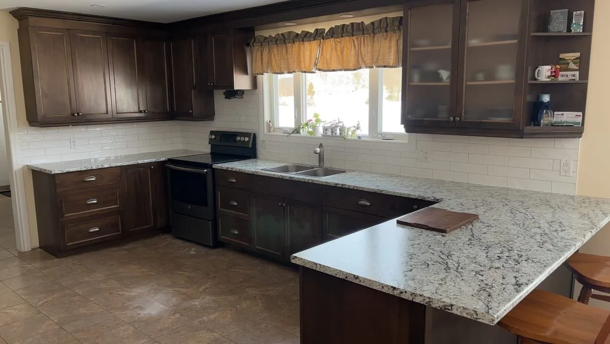 Kitchen with dark wood cabinets, granite countertops, white subway tile backsplash, and a window above the sink with a yellow valance.