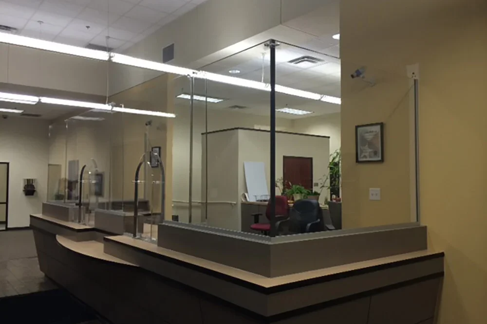 Image of a bank teller window with plexiglass dividers in an empty bank lobby.