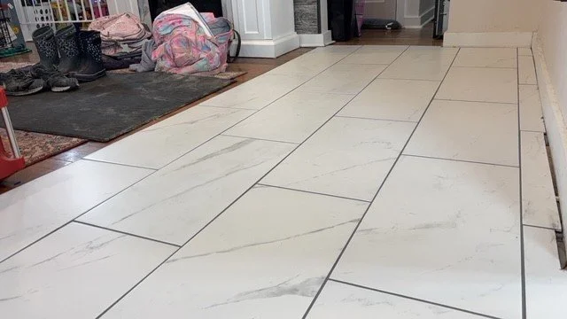 Floor with white marble tiles and a mudroom area with shoes and backpacks.