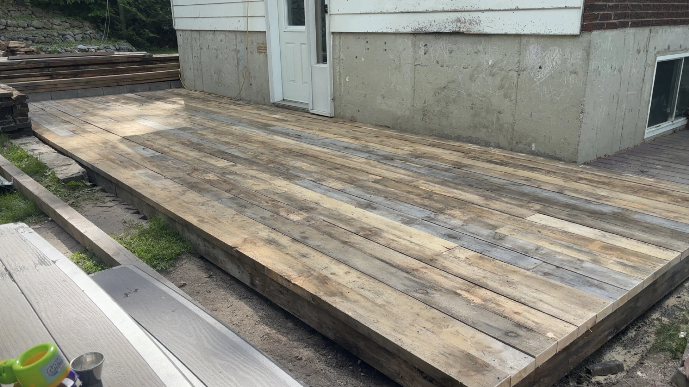 Image shows a wooden deck under construction outside a house, with building materials and tools nearby.