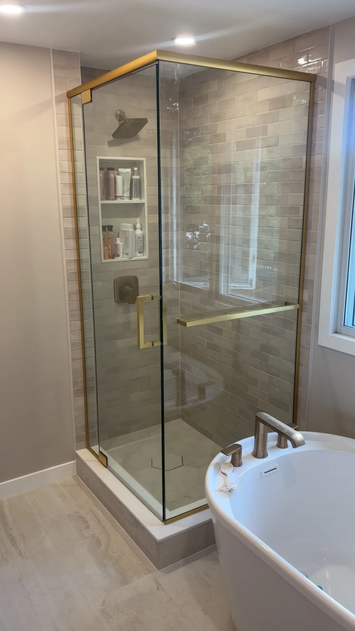 Bathroom with a glass shower enclosure, beige brick wall tiles, and a bathtub with a chrome faucet.