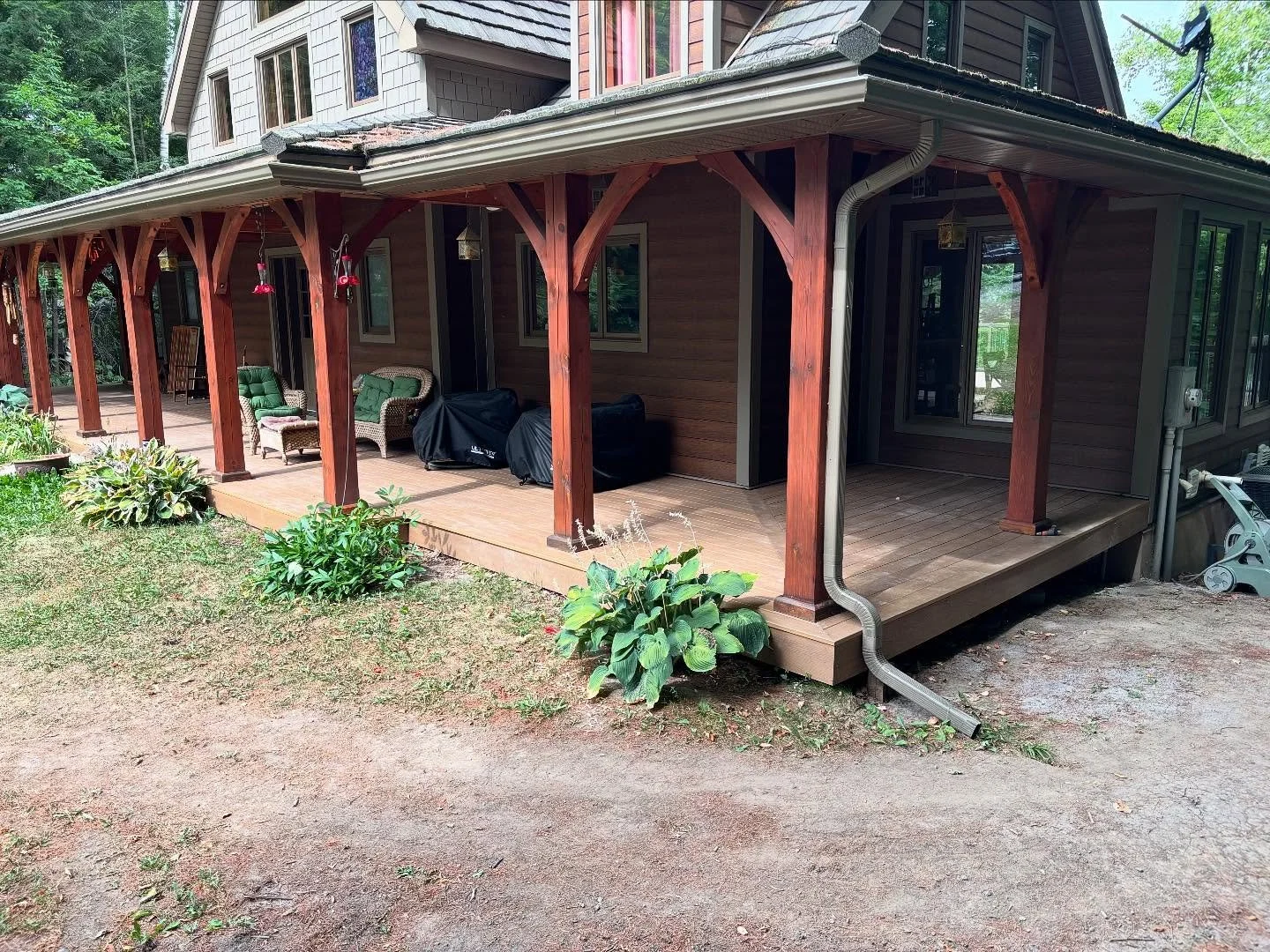 Wooden house porch with outdoor furniture and garden plants, surrounded by trees.