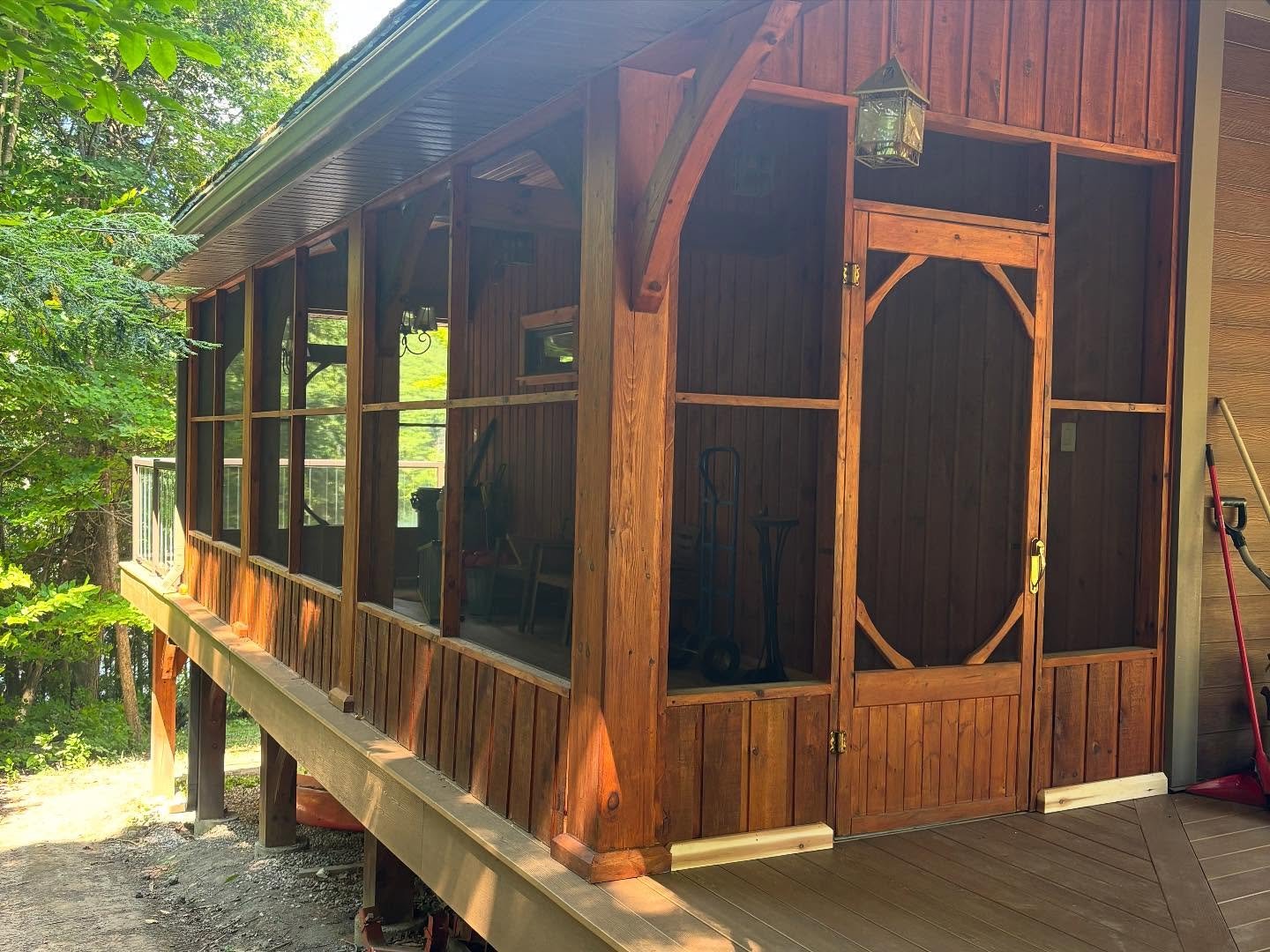 A screened porch attached to a wooden house, with a door, window, and outdoor cleaning tools visible.