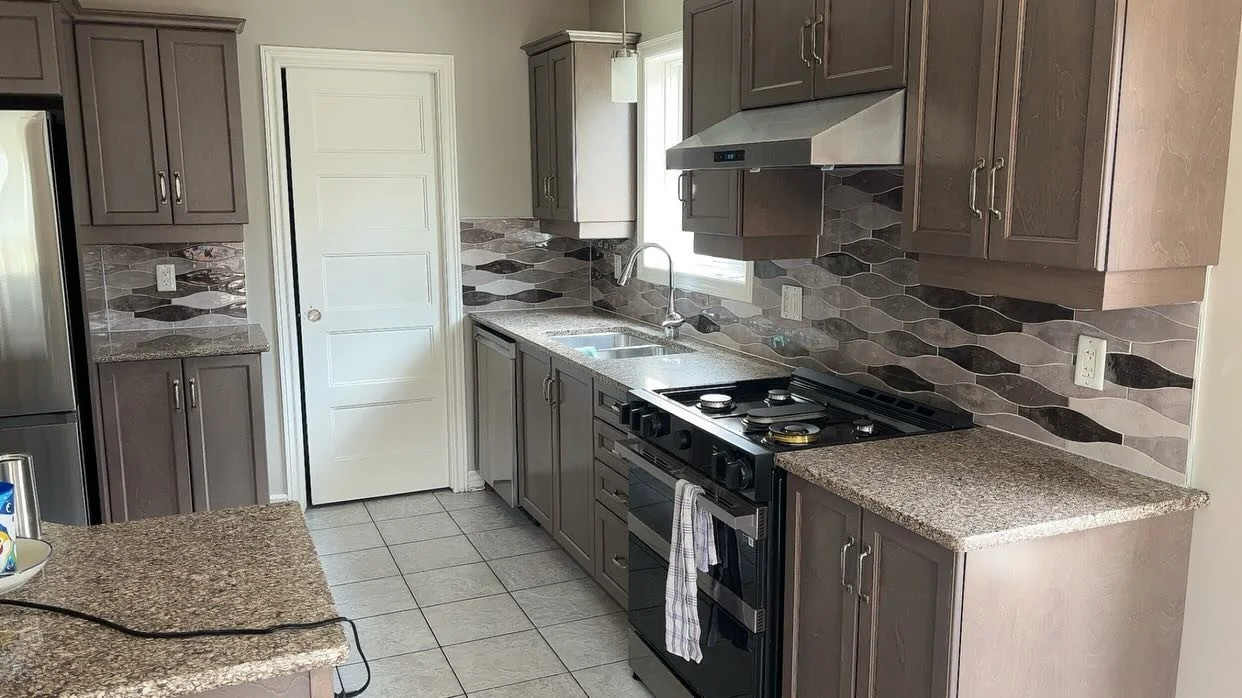 Kitchen with gray cabinets, granite countertops, a stainless steel refrigerator, stove, window above the sink, and a tiled backsplash.