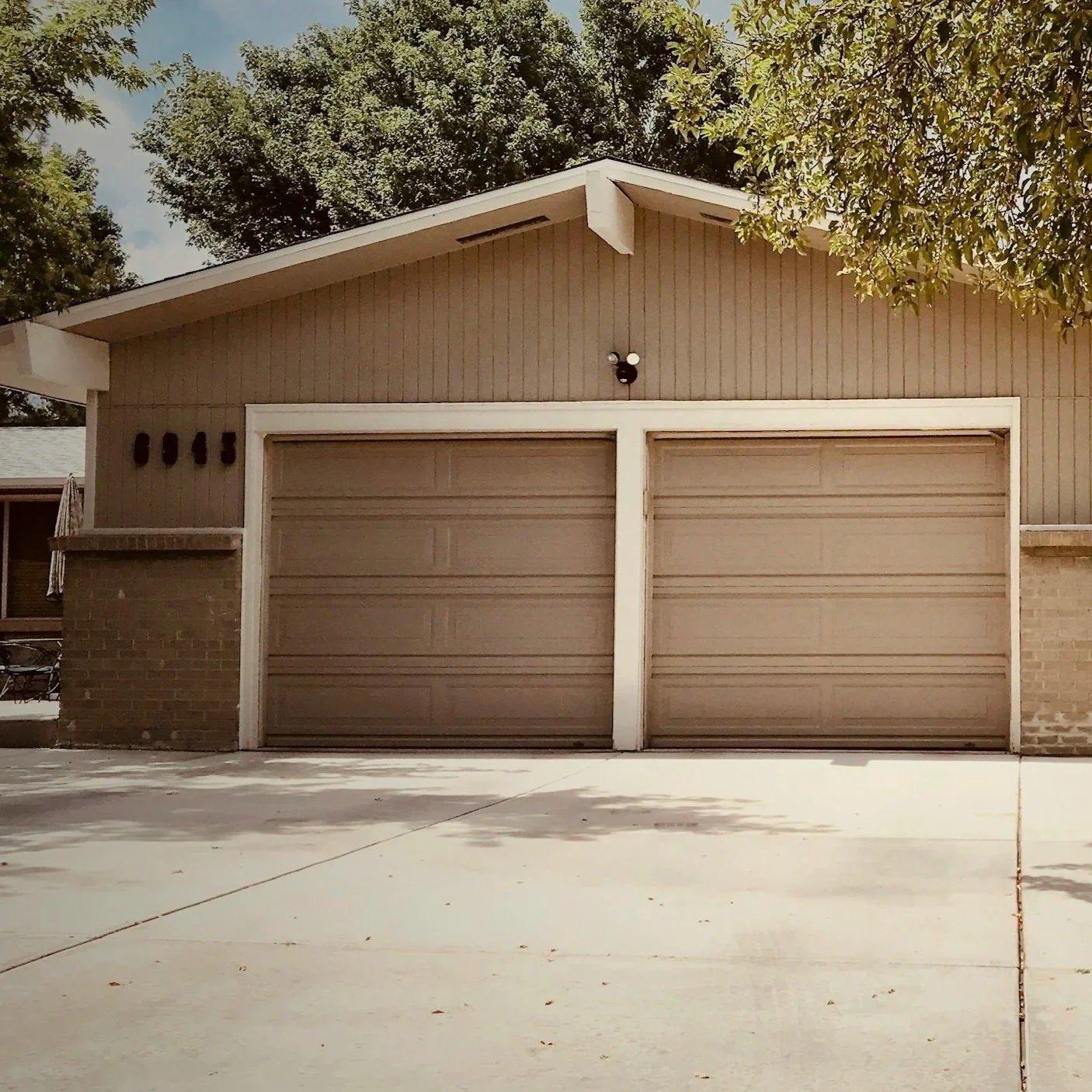 Exterior view of a house with two closed garage doors, a brick and wood facade, and a tree with green leaves in the front yard.