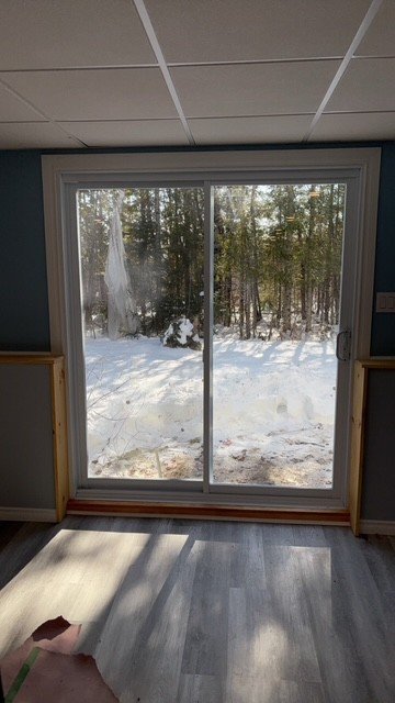 Interior view of a room with a sliding glass door leading to a snowy outdoor landscape with trees.