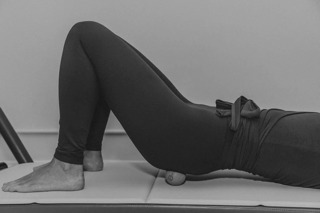 A person performing a shoulder roll on a foam roller, lying on their back with shoulders on the roller, in a fitness or therapy setting.