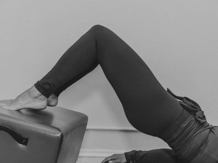 A person lying on the floor with their legs elevated, one foot resting on a box, practicing a yoga pose.