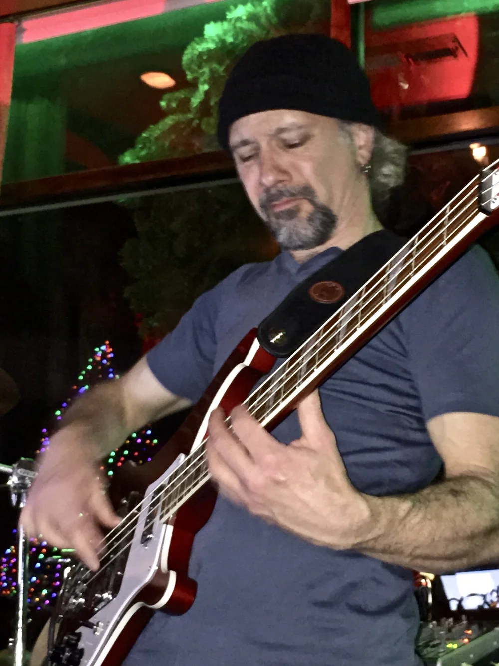 A man playing an electric guitar in a dimly lit venue with colorful Christmas lights and festive decorations in the background.