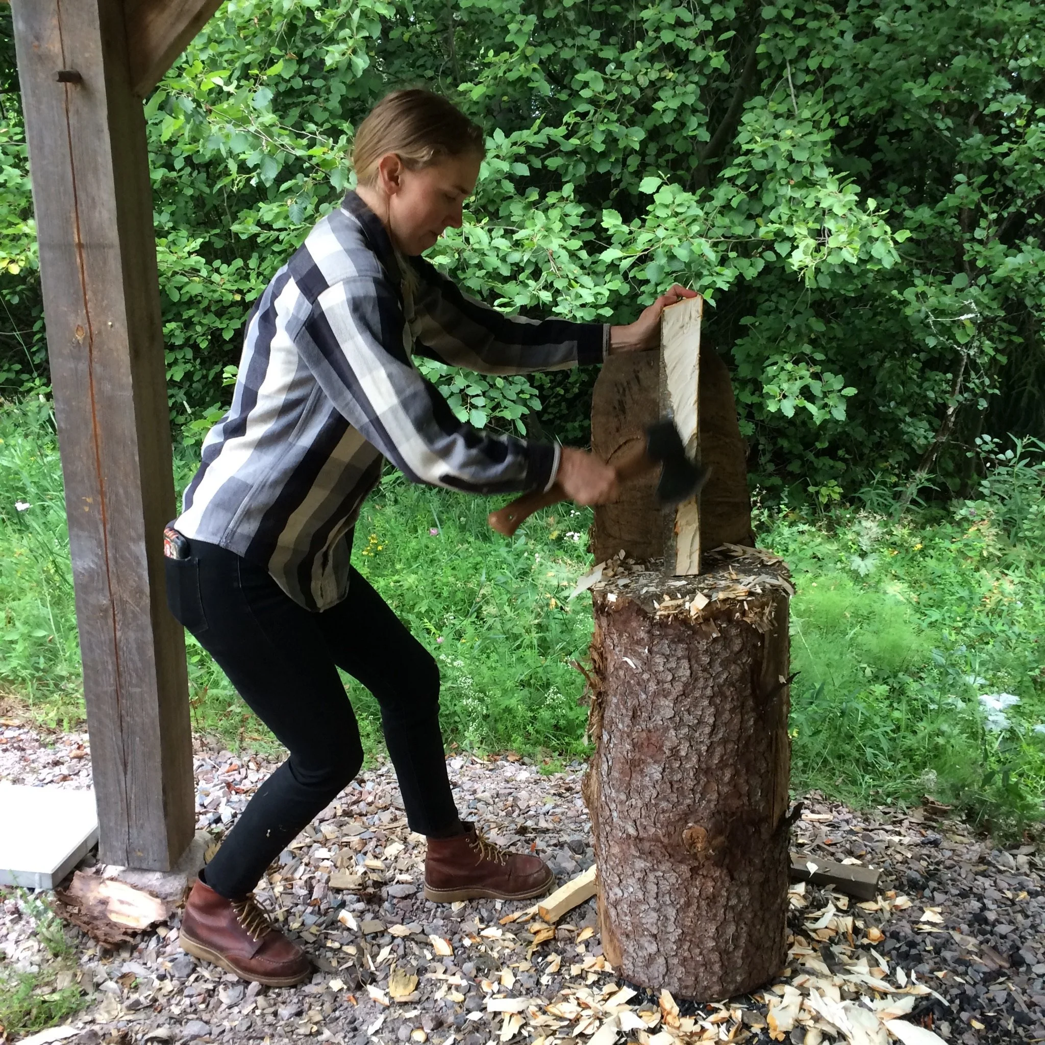 Person with axe, mid chop at a chopping block, with a canopy of green leaves behind