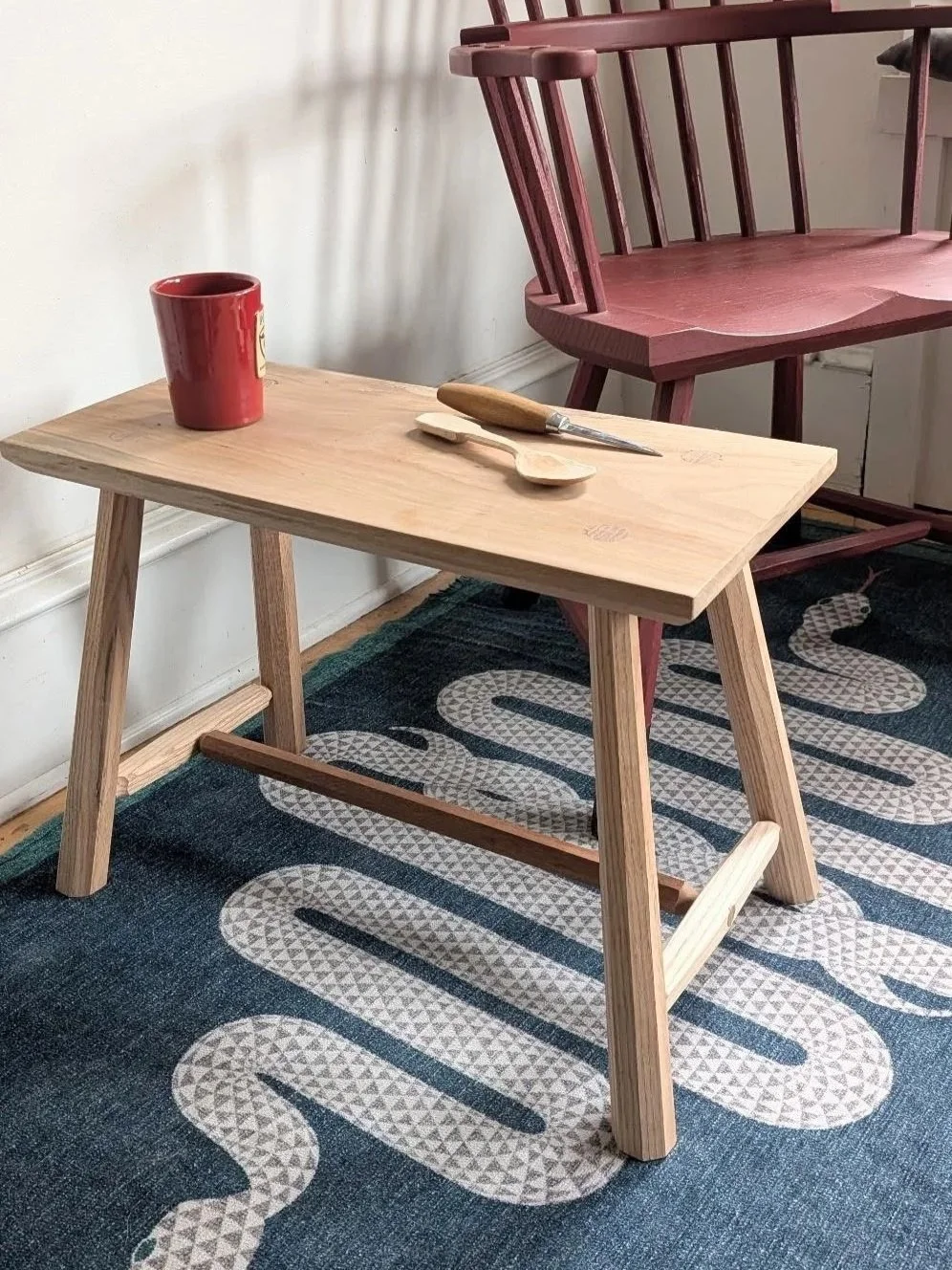 A side table made of light wood on a blue rug with a snake motif.
