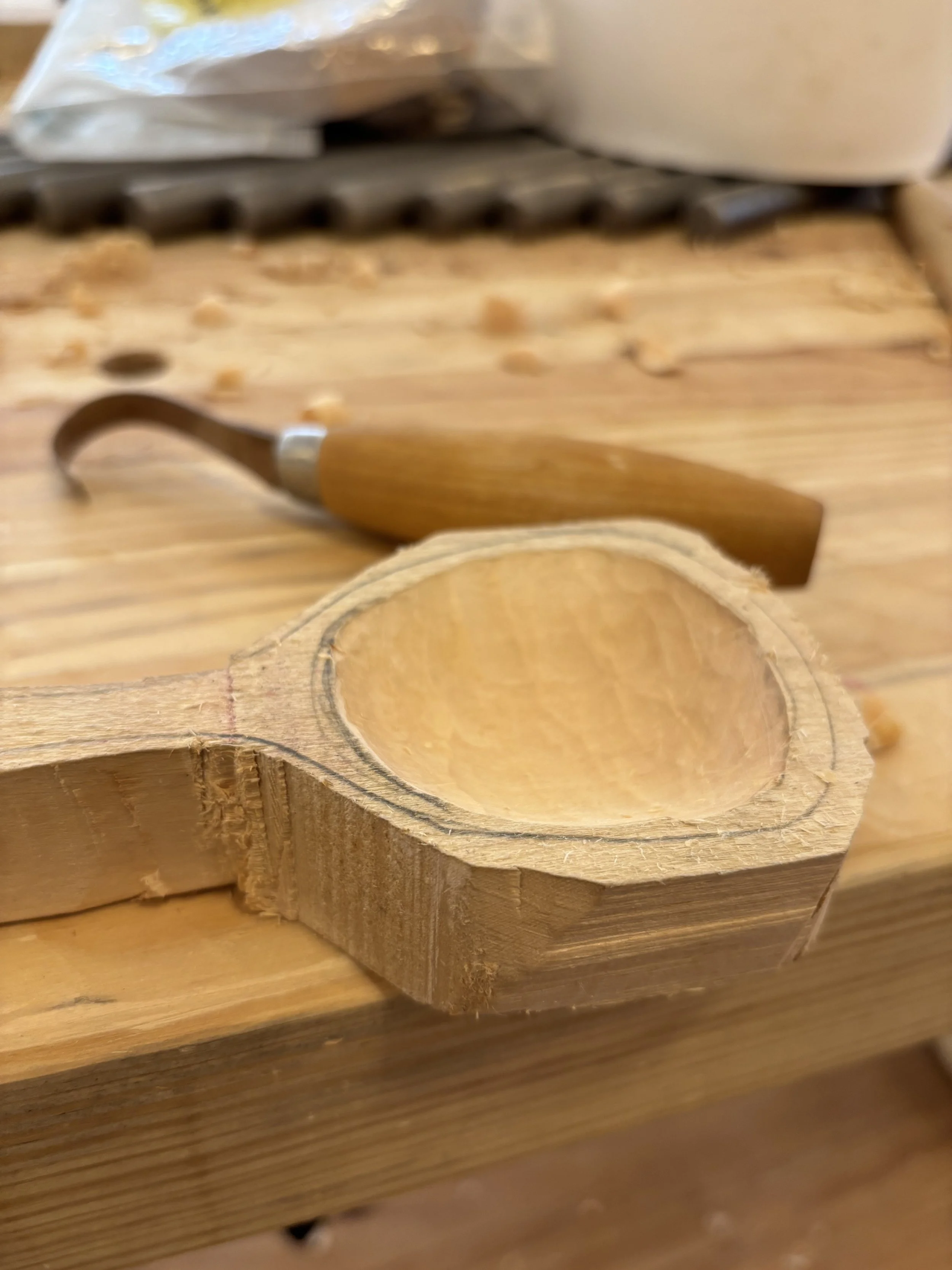 Wooden spoon blank with pencil marking the bowl; hooked carving knife in the background