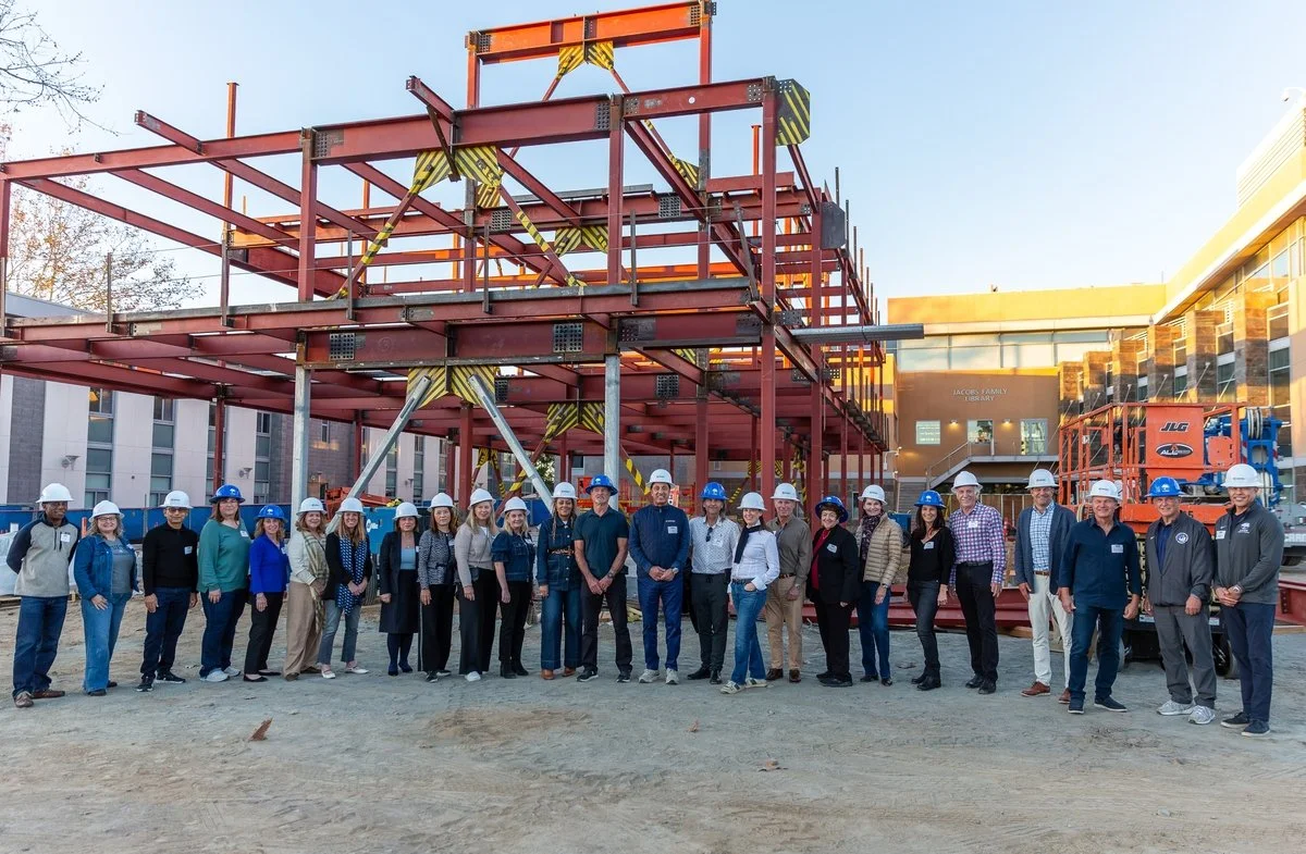 Group of people wearing construction helmets standing in front of a building under construction with steel framework.