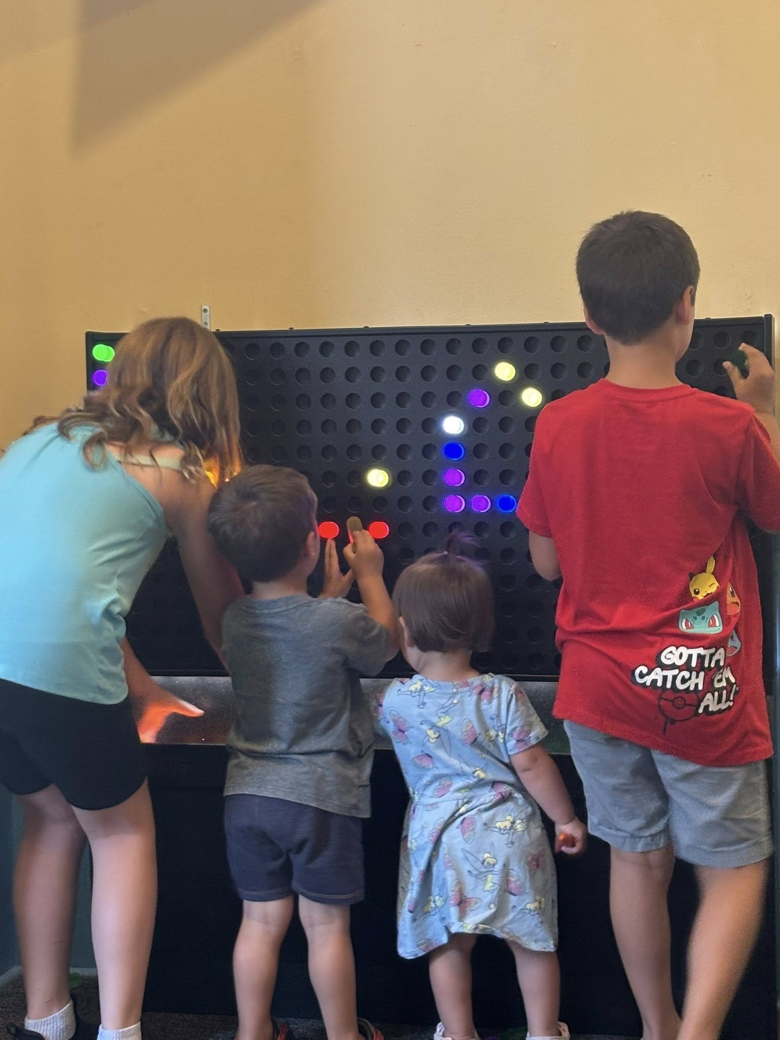 Children and an adult playing a giant Connect Four game with colorful discs.