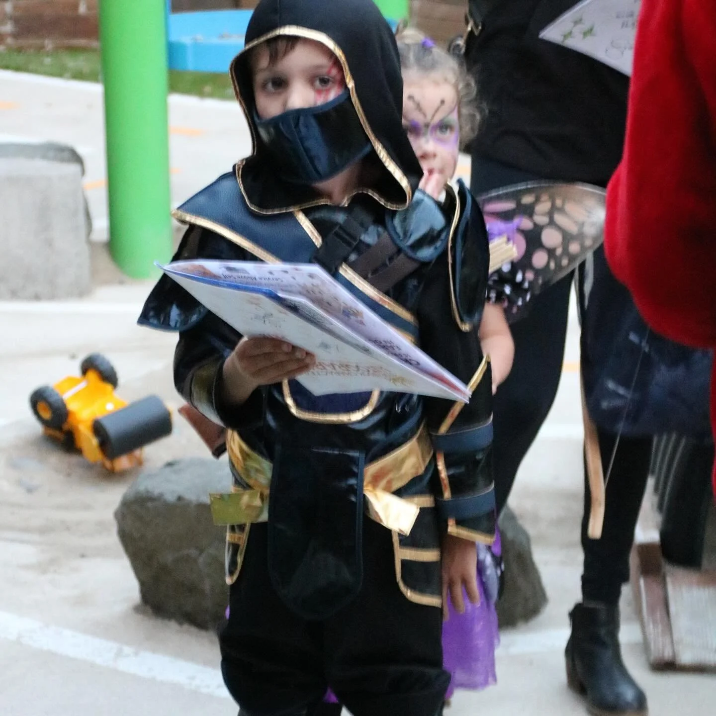 A child in a black and gold ninja costume reads an adventure map during a costume-themed private event.