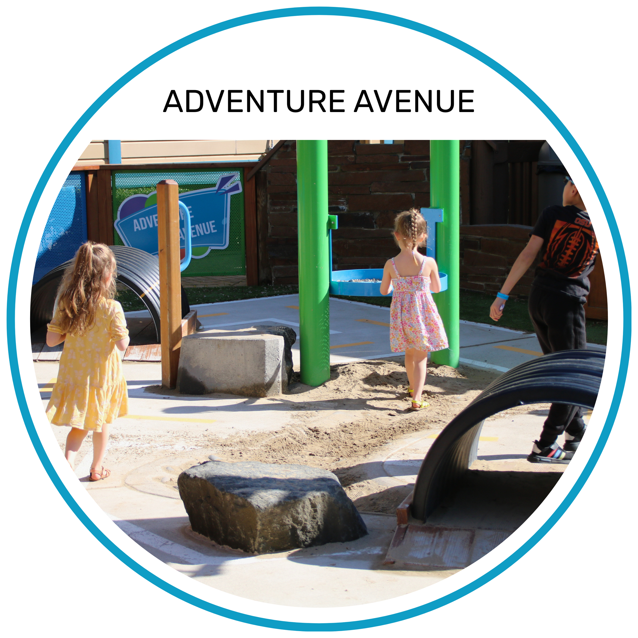 Children playing on a playground at Adventure Avenue, with a slide, rocks, and sand, surrounded by a fence.