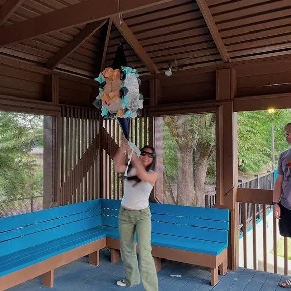 A graduate swings at a star piñata in the museum gazebo during a private evening graduation party.