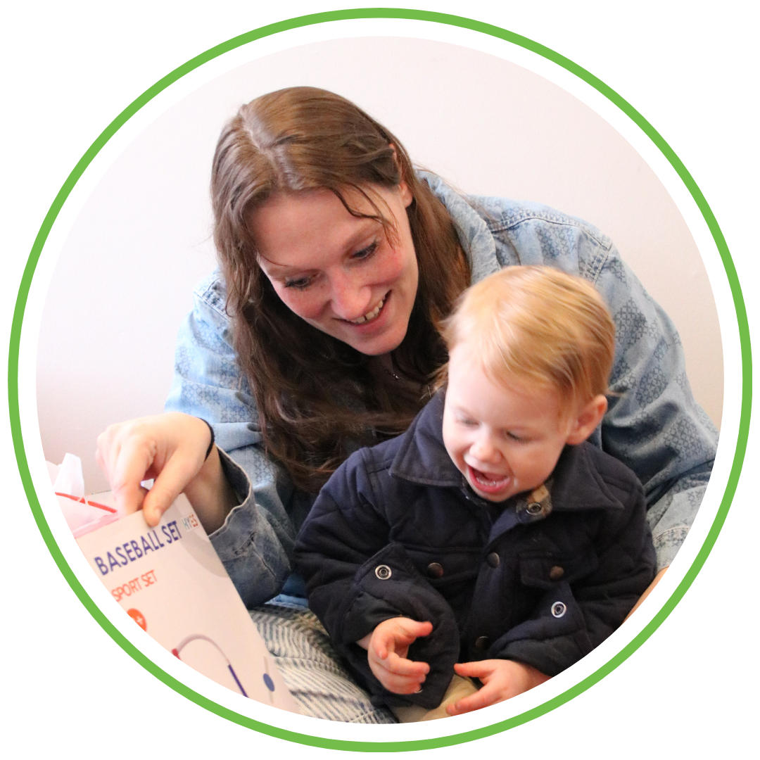 A woman and a young boy smiling and playing with a baseball set.