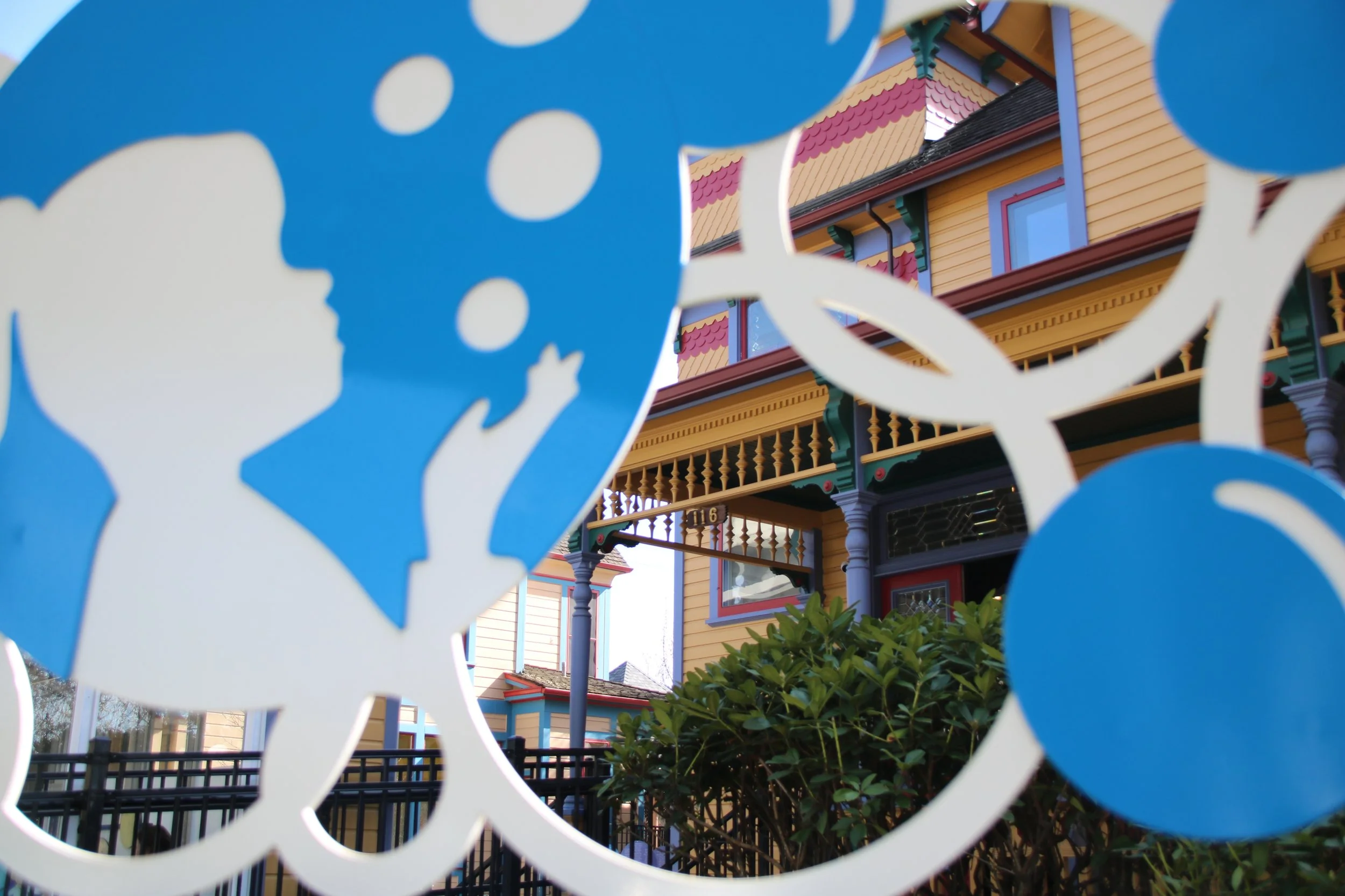 Colorful Victorian-style house viewed through a decorative white and blue paper cutout with a silhouette of a child blowing bubbles.