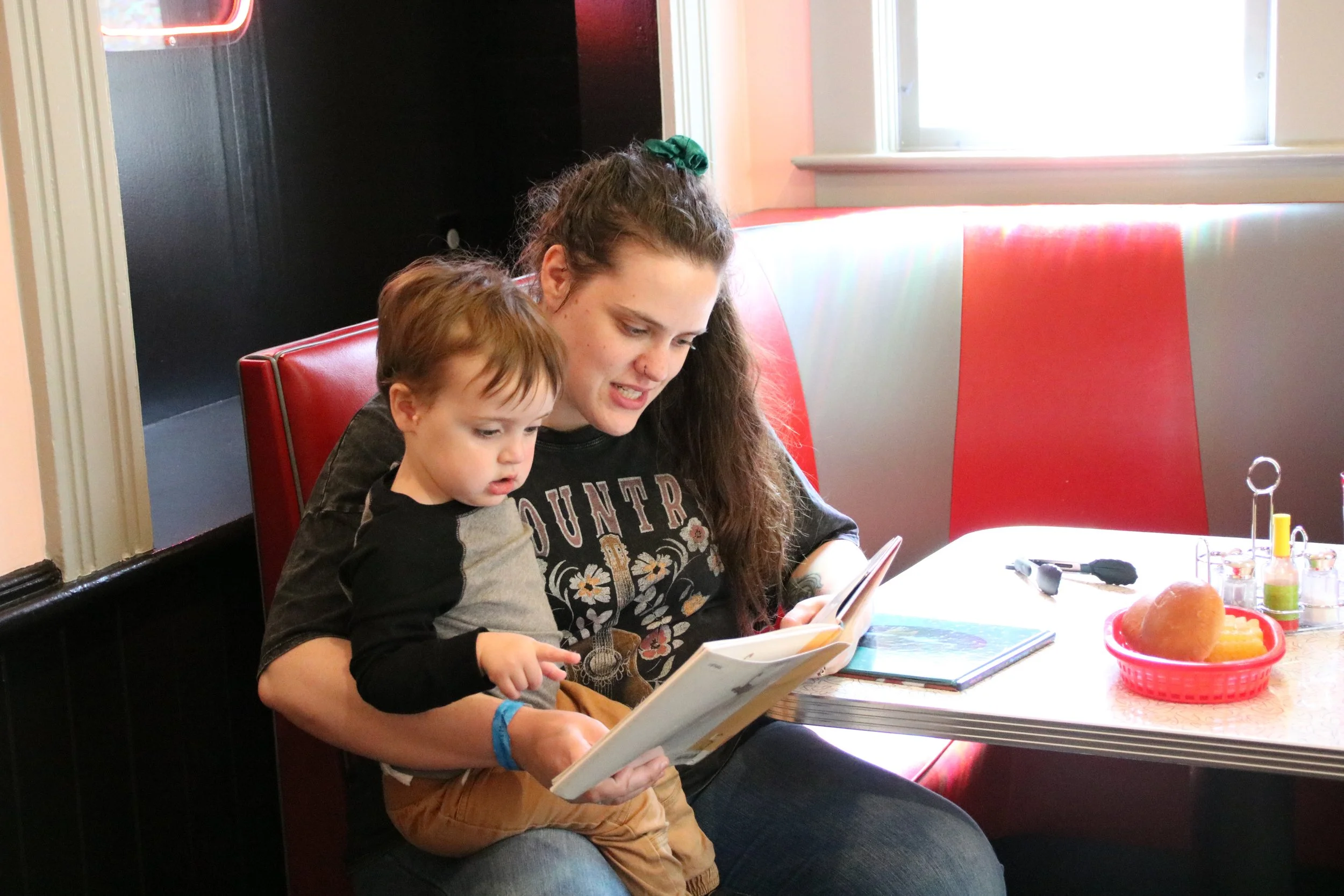 A young woman and a small child sitting at a diner booth, looking at a menu.