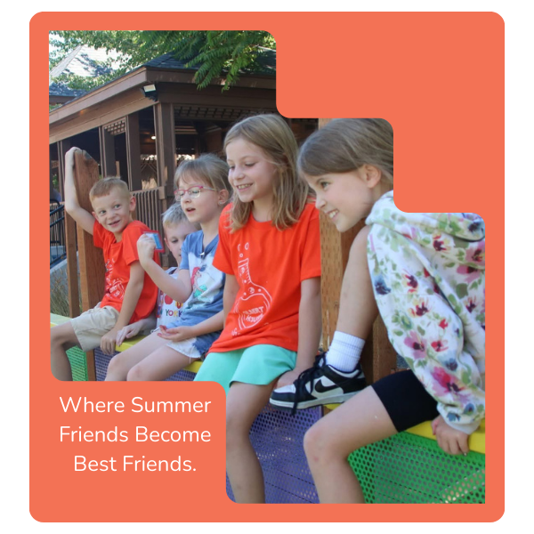 Group of five children sitting on a bench outside, smiling and talking, with a wooden house and trees in the background, enjoying a sunny day.